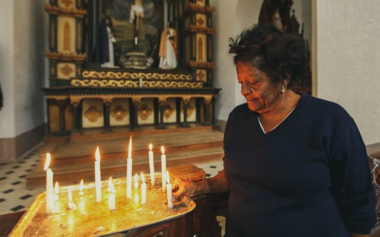 An elderly woman lights candles in a church, symbolizing devotion and spirituality.