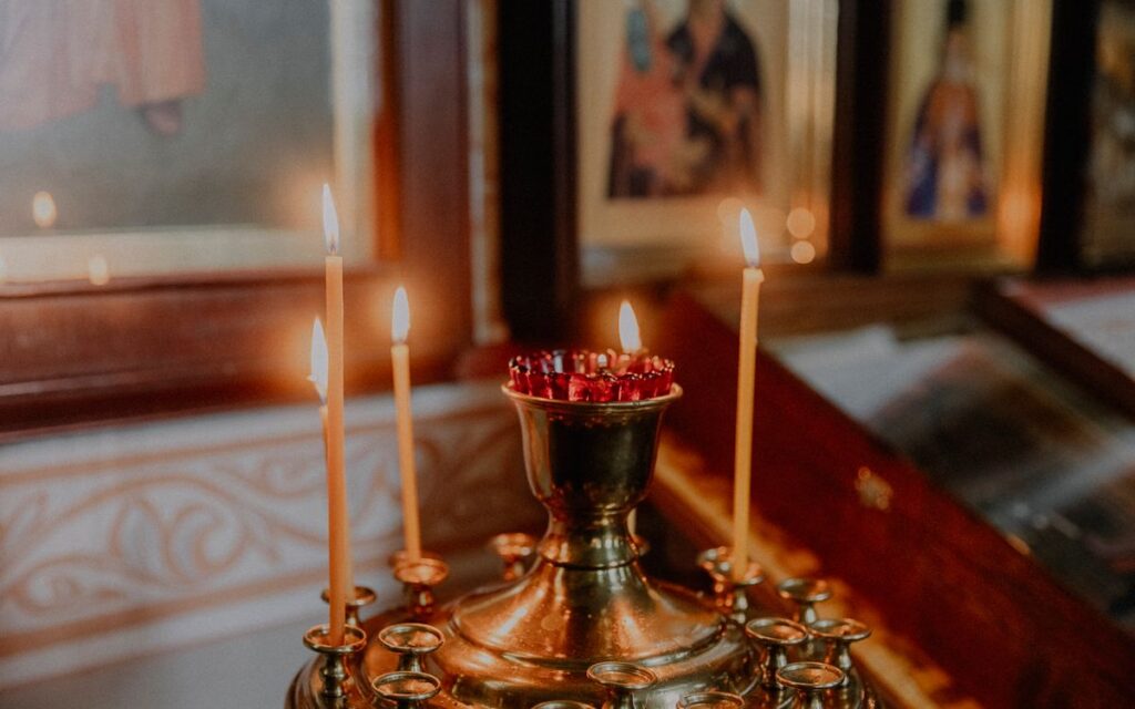 Softly lit church candles next to orthodox icons creating a warm, spiritual ambiance.
