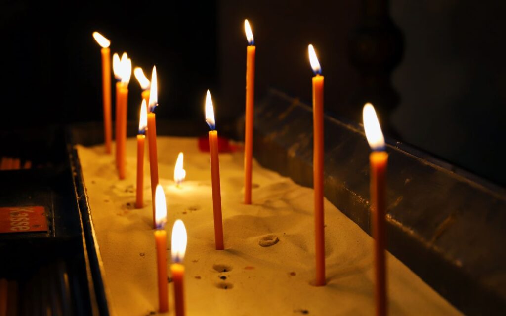 Illuminated votive candles in sand create a serene spiritual ambiance in a dimly lit setting.