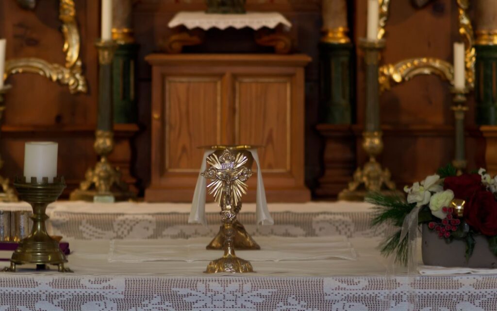 Close-up of a church altar featuring a chalice, candles, and floral decorations.