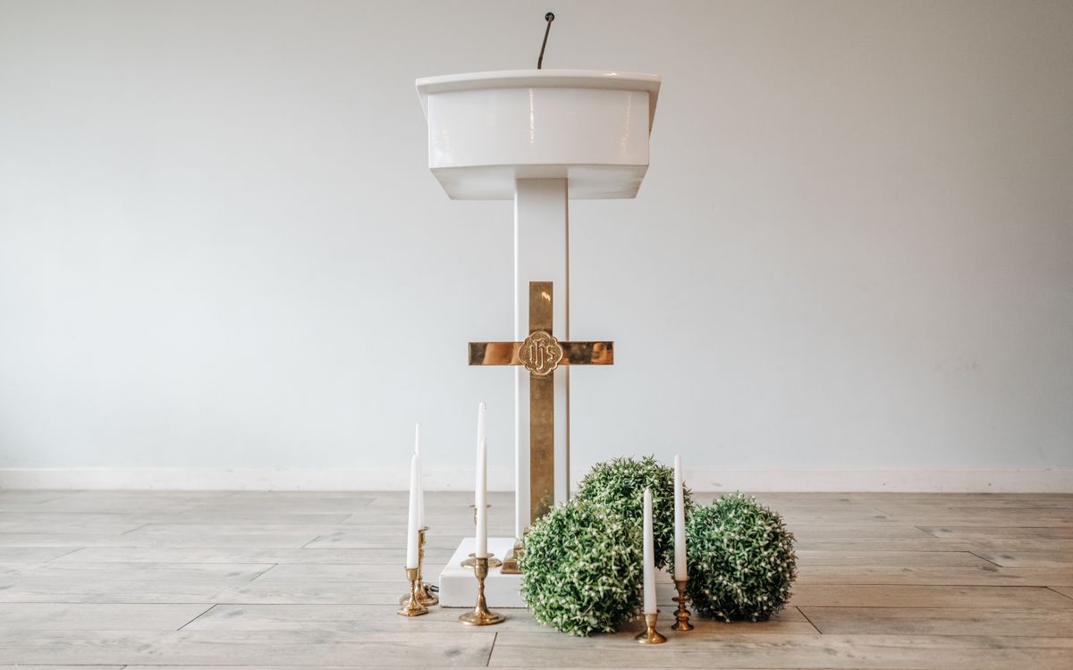 A minimalistic church altar setup featuring a white podium, golden cross, and decorative candles.