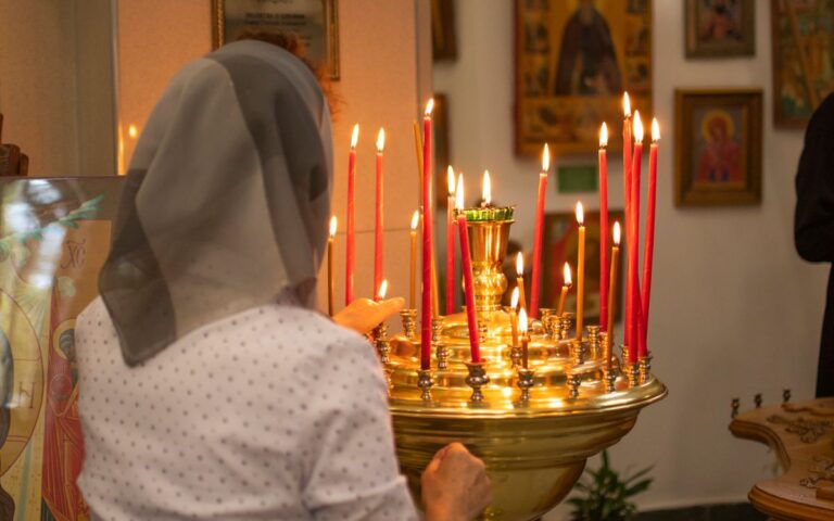 A woman lights candles in a church, highlighting religious devotion and tradition.