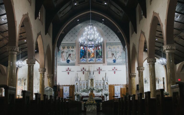 Intricate interior of a historic church with stunning stained glass, arches, and chandeliers.