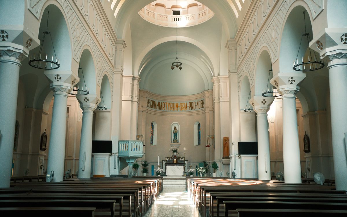 Sunlit interior of a grand Catholic church with elegant arches and stone columns.