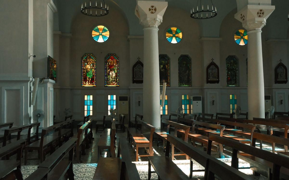Sunlit church interior with stunning stained glass windows and wooden pews.