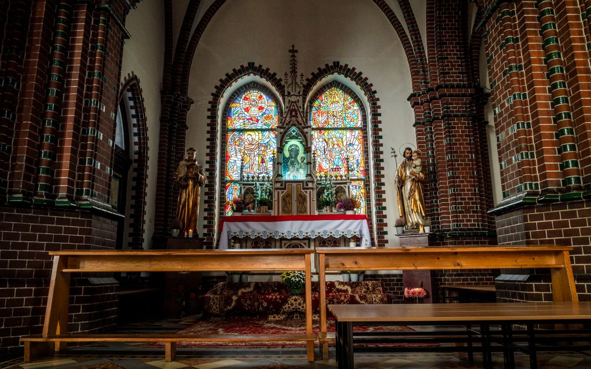 A serene view of a church altar featuring stained glass and statues.