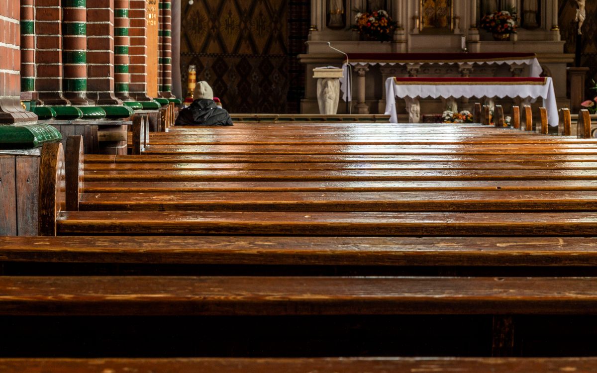 Empty church interior with wooden pews leading to richly decorated altar, warm atmosphere.