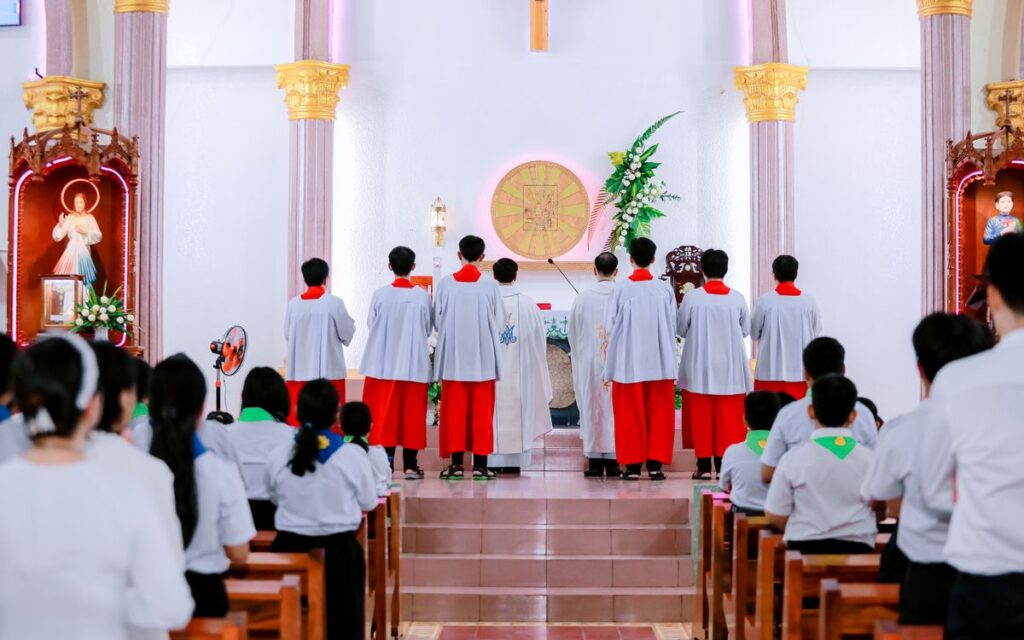 Catholic mass with altar servers and congregation inside a church.