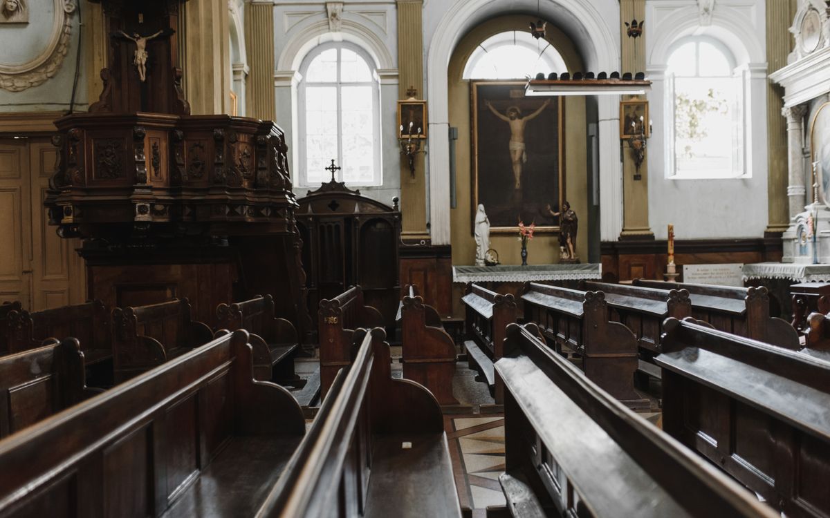 Elegant church interior showcasing wooden pews, religious icons, and natural light from large windows.