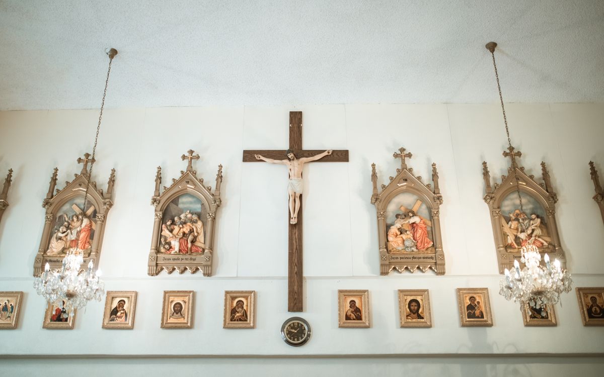 Church interior showcasing wall-mounted crucifix and religious icons under chandeliers.